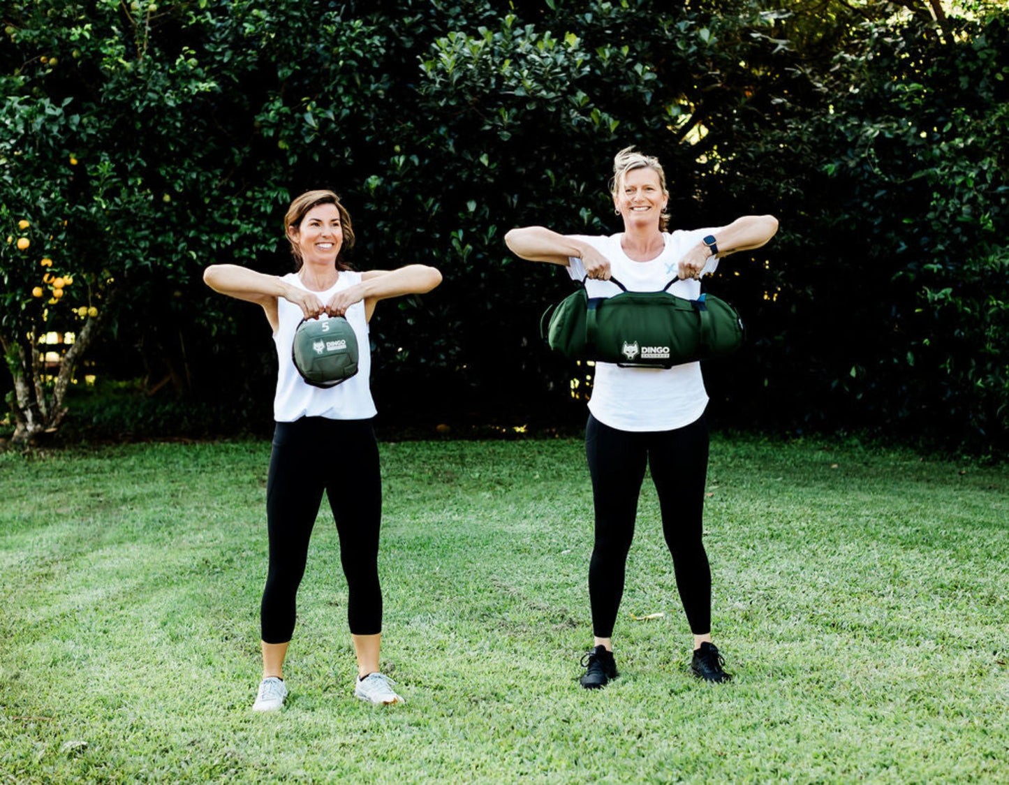 Two women exercising outdoors with dingo sandbags
