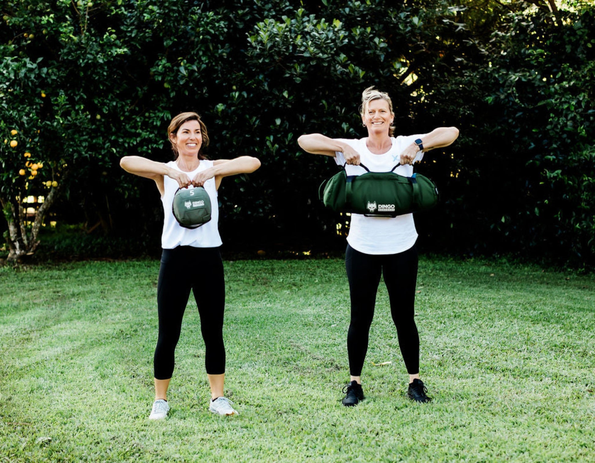 Two women exercising outdoors with dingo sandbags 